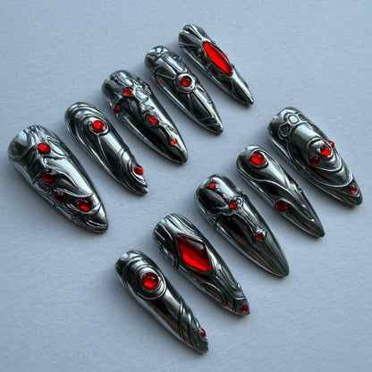 Metallic nail art tips with red gemstones on a gray background