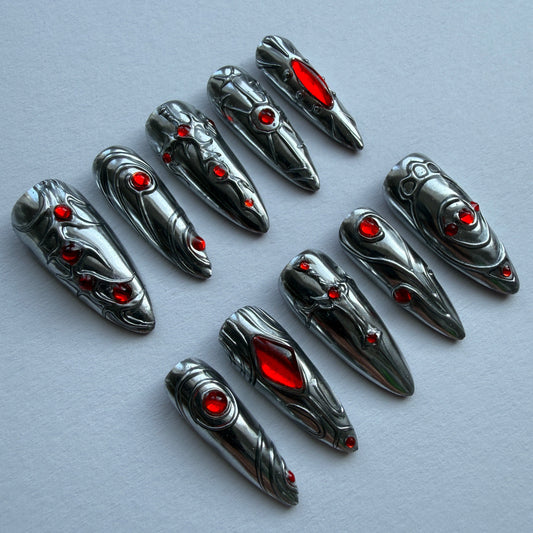 Metallic nail art tips with red gemstones on a gray background